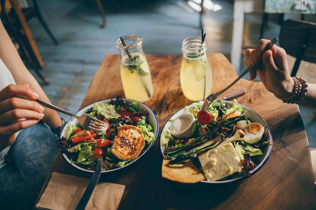 Two people sitting across from each other at a small table, eating healthy meals and drinking refreshments out of glass jars.