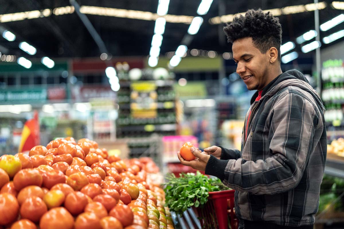 Young adult looking at tomatoes while in the produce section at a grocery store.