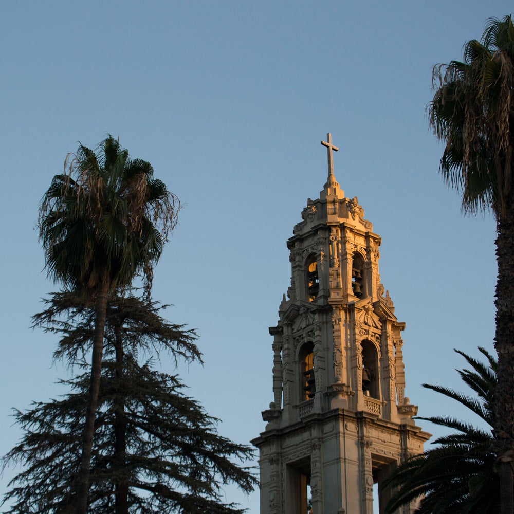 Historic cross-topped building in Downtown Riverside surrounded by tall trees.
