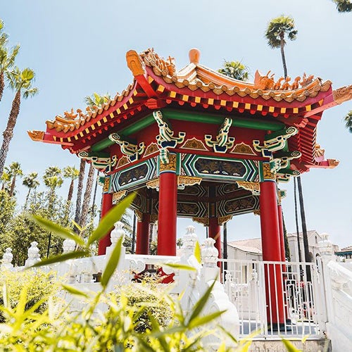 Three UCR students taking a hike along a dirt trail that is surrounded by large rocks and green grass.