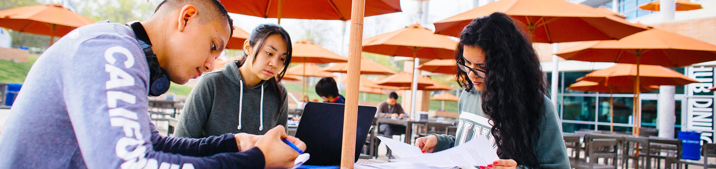 Three students gather to study at a table outside the Highlander Union Building (HUB) on the UC Riverside campus. 