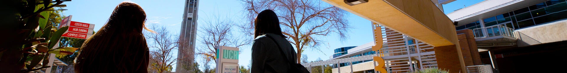 Two students appear as silhouettes while they sit facing toward the Bell Tower on the UC Riverside campus.