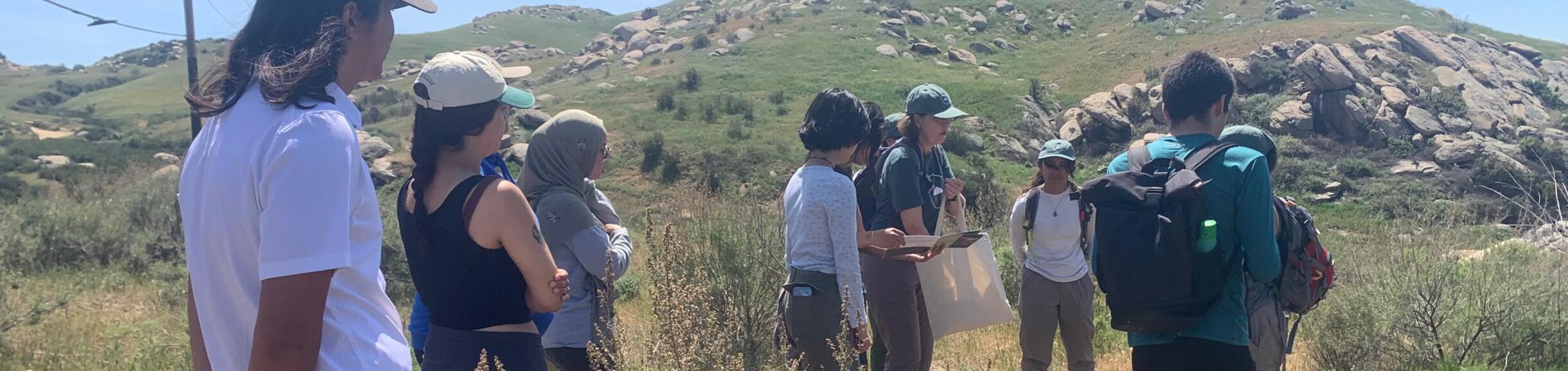 A group of students listen to an outdoor workshop