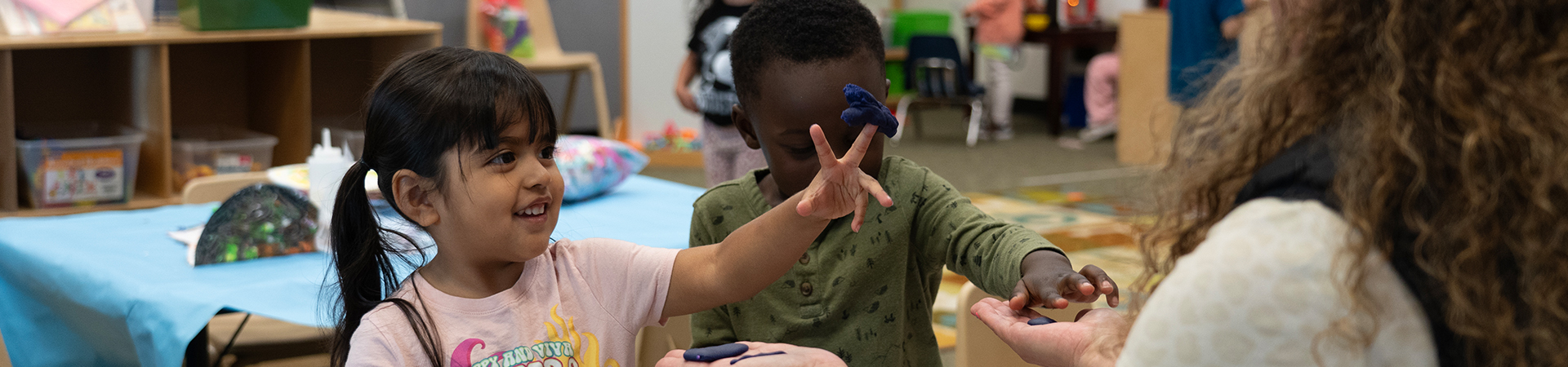 children showing play-dough to teacher