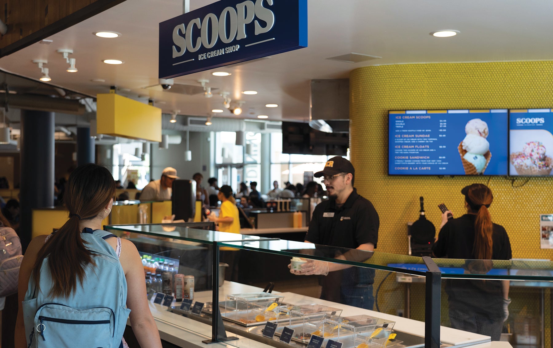 Scoops employee serves ice cream bowl to student