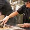 A student worker uses tongs to pick up pieces of chicken.
