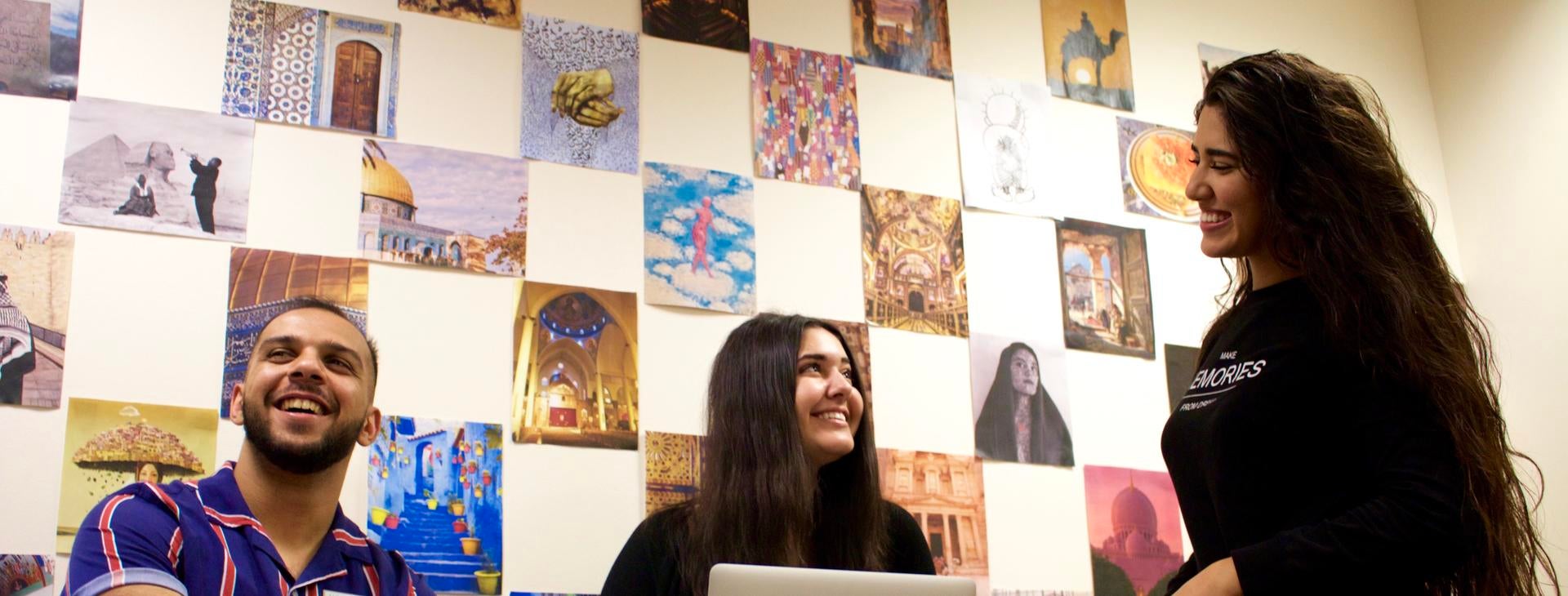 Three students smiling and working on a computer, MESC