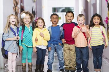 A group of children with backpacks laugh at the camera. 