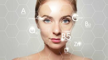 A woman with light skin and blue eyes stares at the viwer. The image is overlayed by a honeycomb pattern with various vitiman letters. 