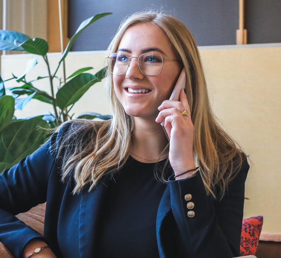 Young White woman smiling at her desk with a mobil phone up to her ear