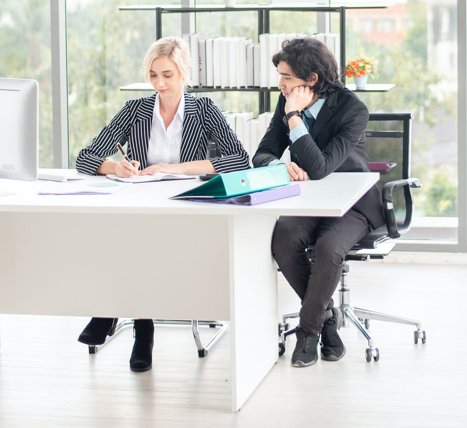 Young White woman and Asian man working at a desk together Monitor paperwork and notebooks on the desk