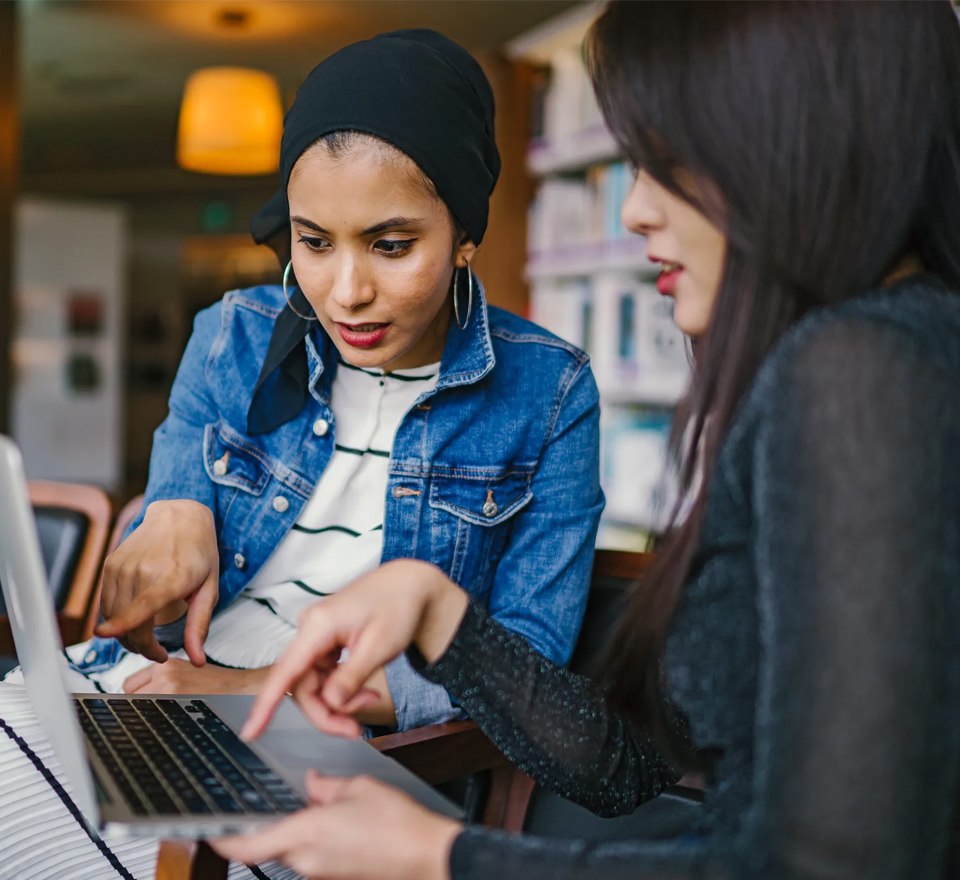 Two young women in casual attire working on a laptop together