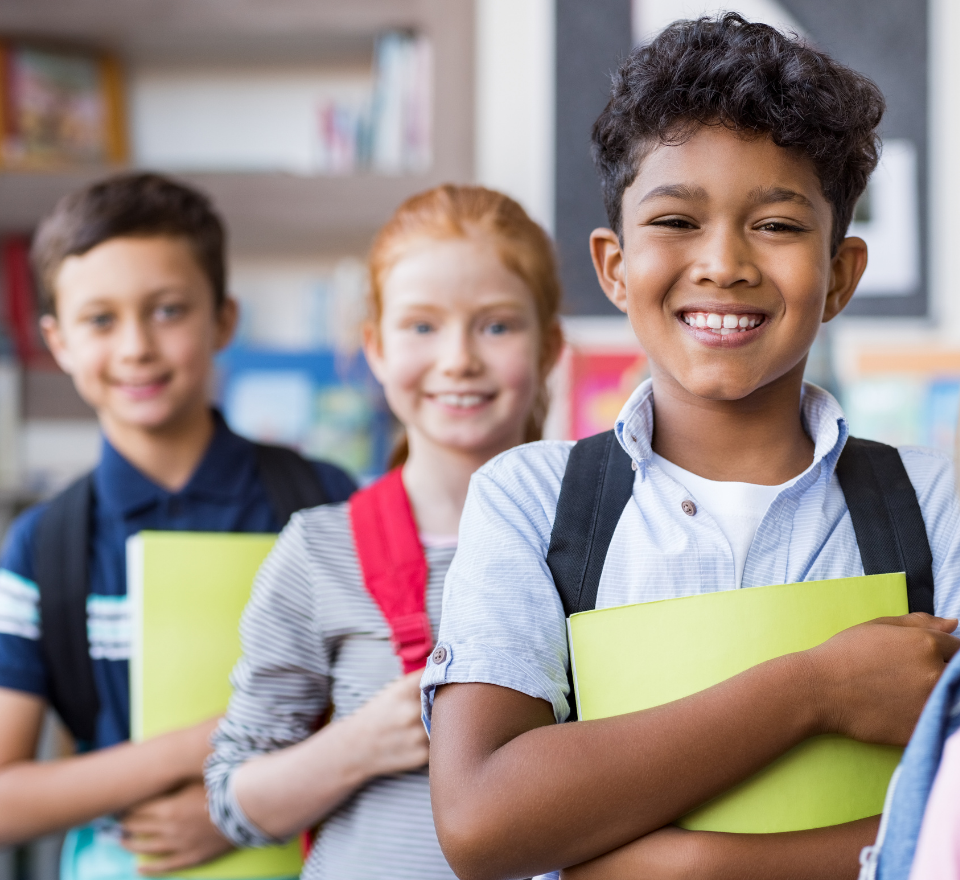 Two young boys and a young girl wearing backpacks and holding school work