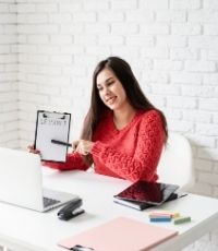 Teacher sitting at desk pointing at Lesson plan in front of computer