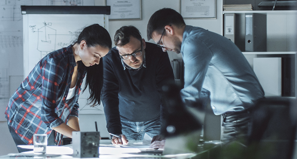 Young woman and man standing on either side of a middle age man all looking down at a diagram together