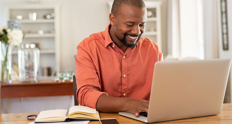 Middle aged Black man smiling while working on his laptop at home