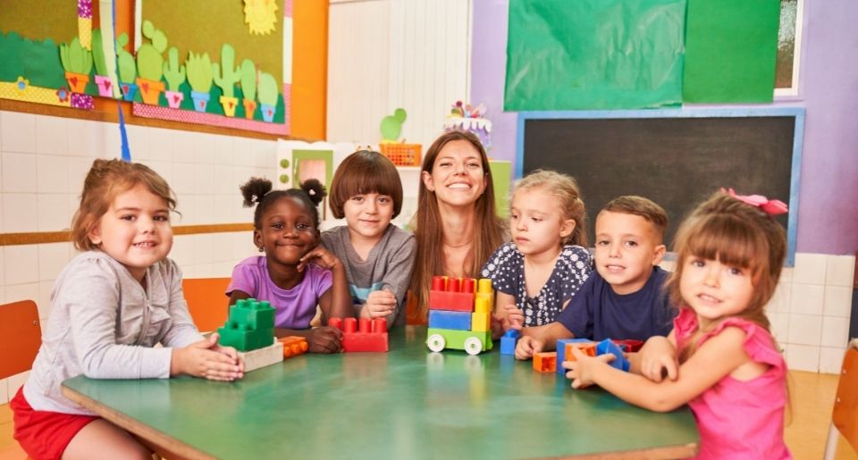 Early childhood education teacher surrounded by young children in her class smiling at the camera