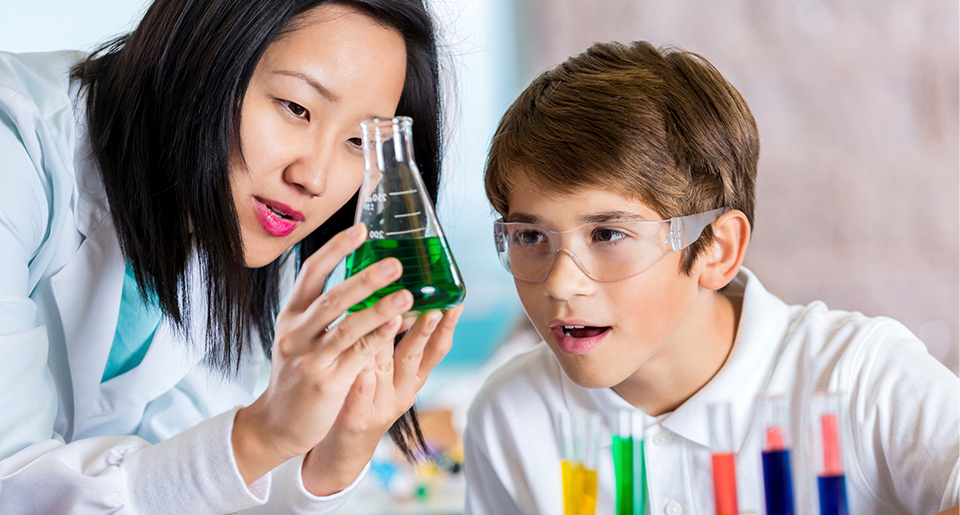 Young Asian female teacher holding a science test bottle and a White middle school boy looking at it with her