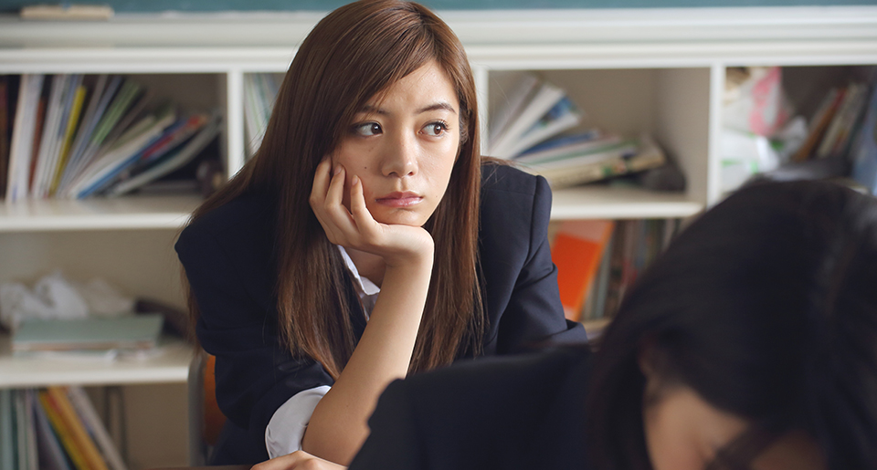 Asian highschool girl with her chin in her hand at her desk looking sad