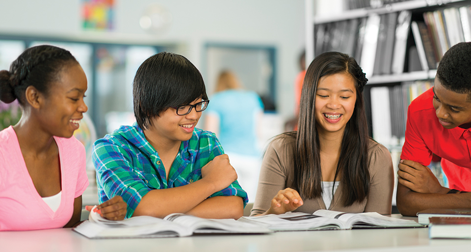 Diverse group of 4 highschool student smiling and looking down at something