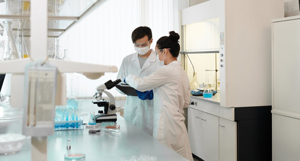 Professional man and woman in lab coats looking at a microscope