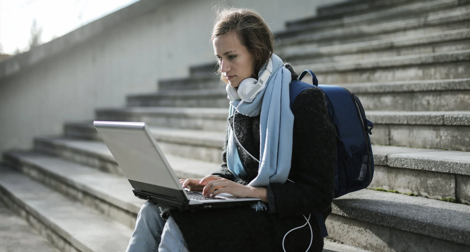 Young female student studying on laptop on a set of stairs outside