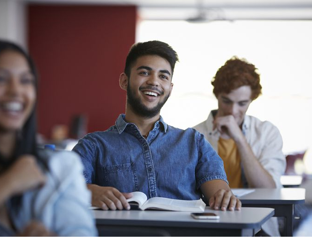 Classroom showing 3 diverse students smiling and listening to a lecture
