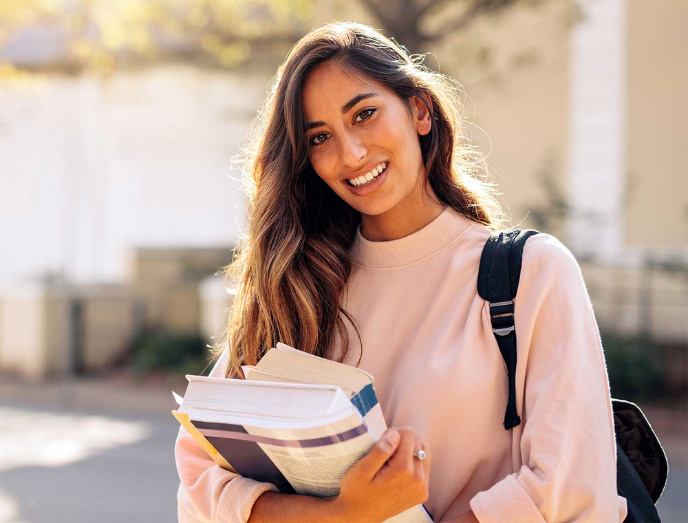 College age Hispanic woman standing outside holding books