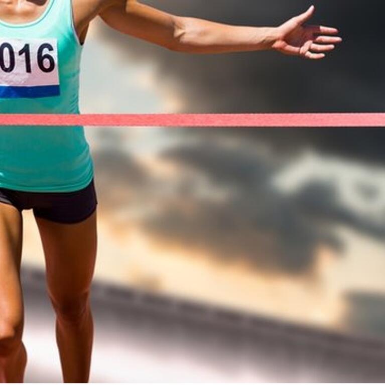 A runner with arms spread out and just about to break the ribbon while crossing a finish line