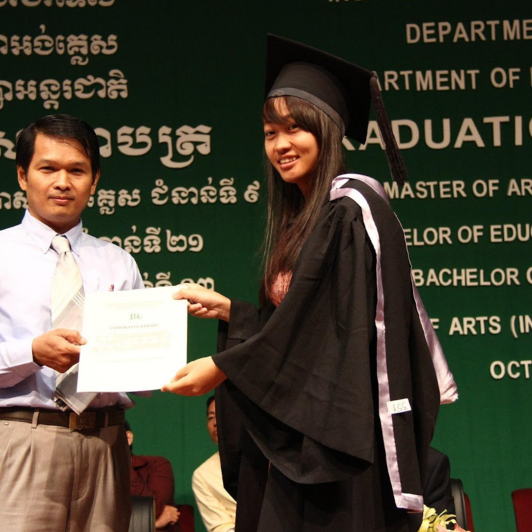 An official and a graduate are holding a certificate together against a green background that reads “Graduation Ceremony” and “Master of Arts (TESOL)”