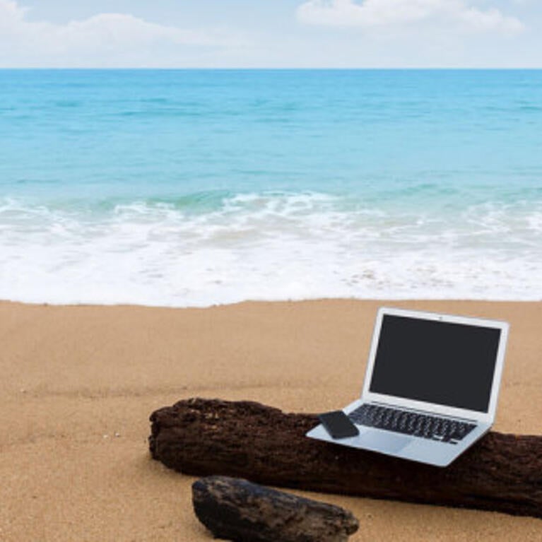 Two gray laptops and a black phone sitting on a log on a beach