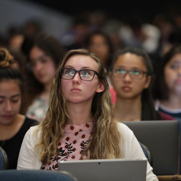 A student sits in a lecture room surrounded by other students