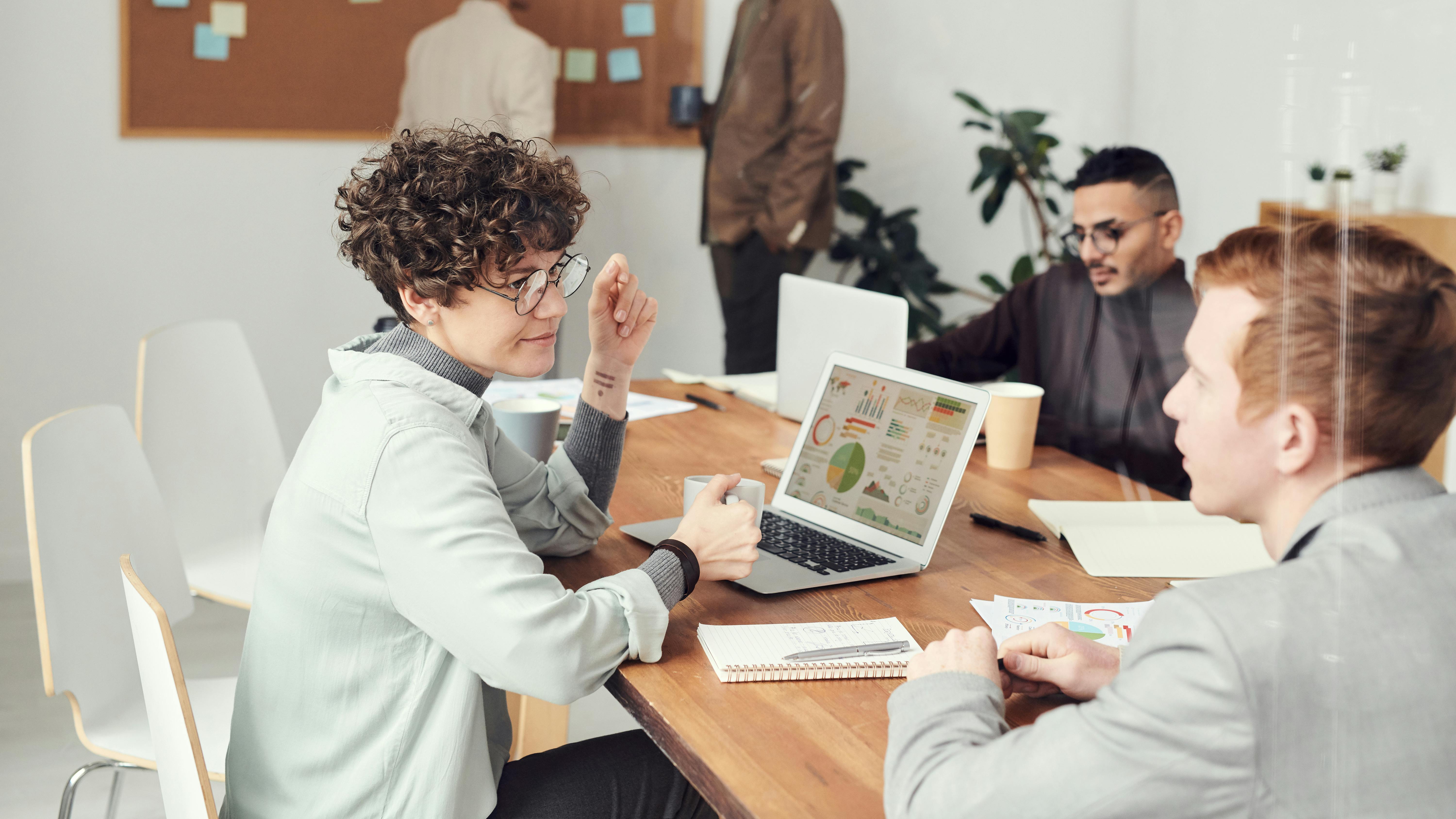 A meeting where a woman is talking to another man while looking at a laptop