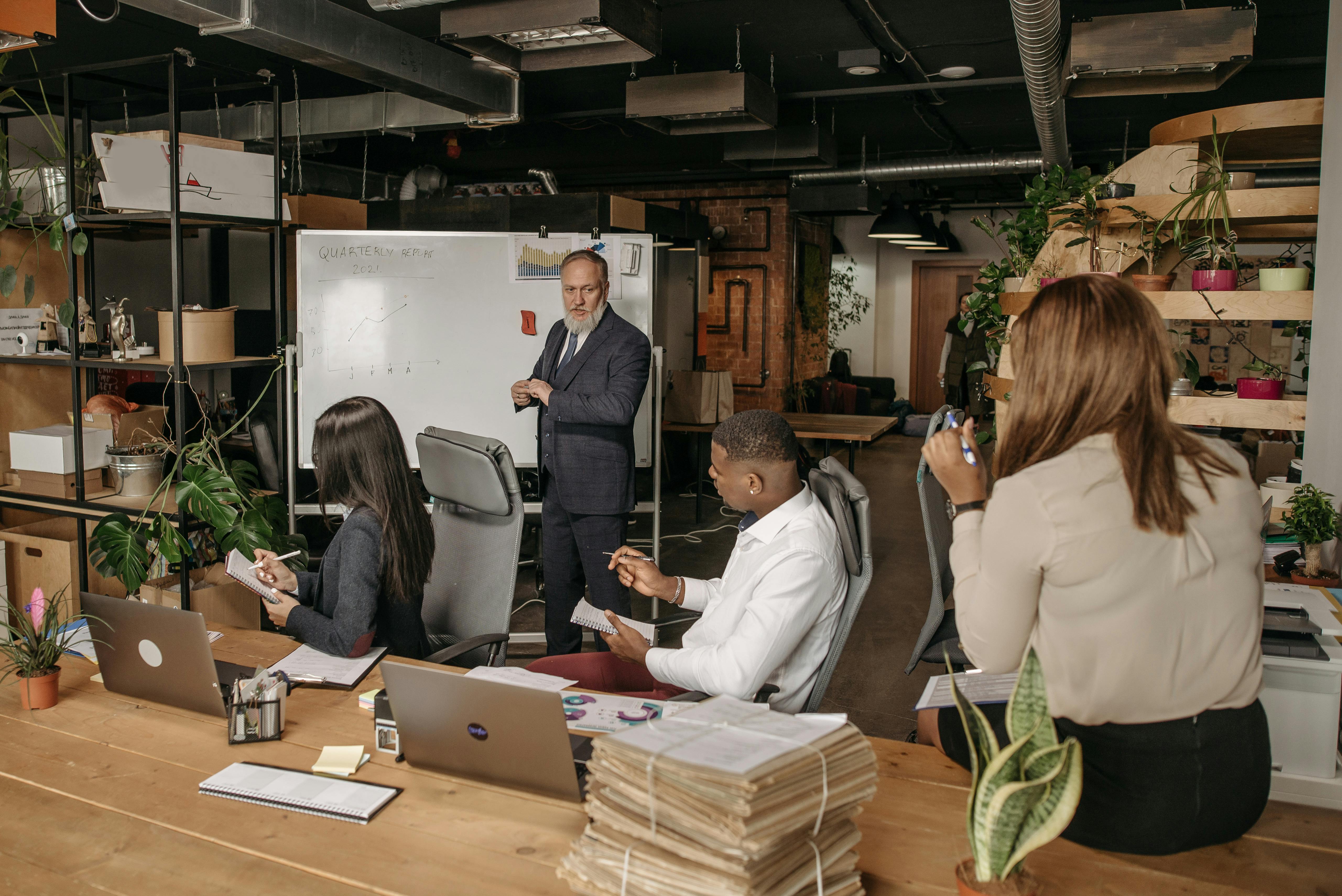 A man leading a meeting while three employees are taking notes
