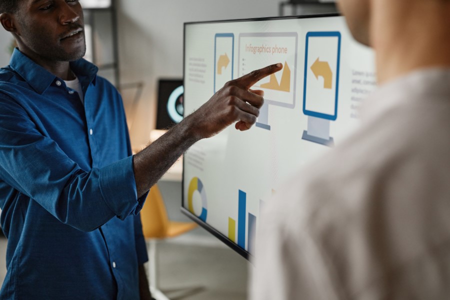 A man pointing to a computer screen that is displaying graphs while another man watches