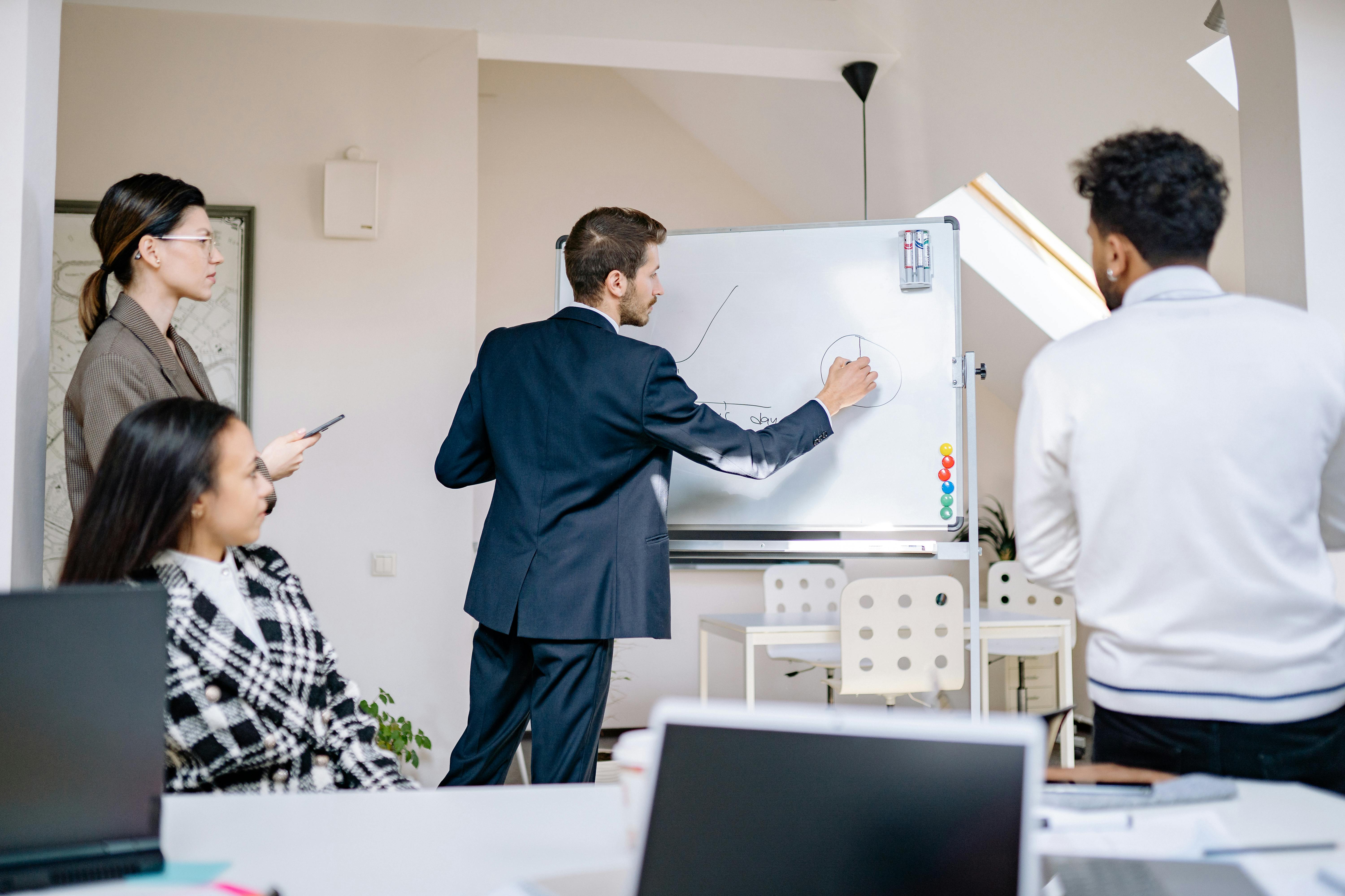 A man writing on a white board while his colleagues watch