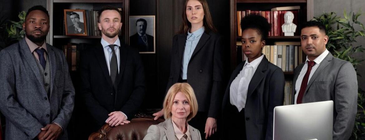 A diverse group of men and women professionally dressed standing and sitting in a professional office.
