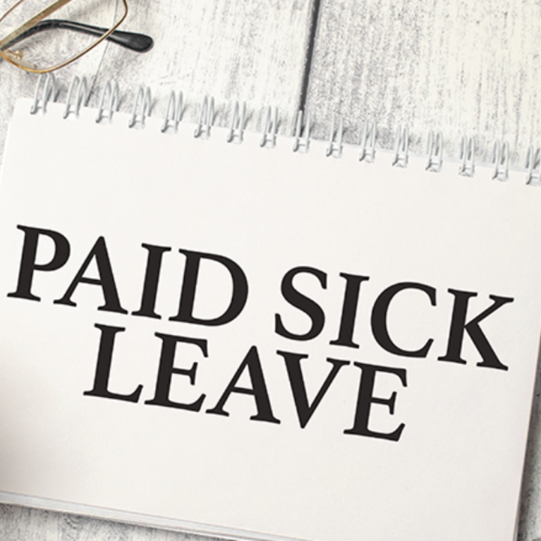 a notepad that states paid sick leave with a pen and glasses next to it