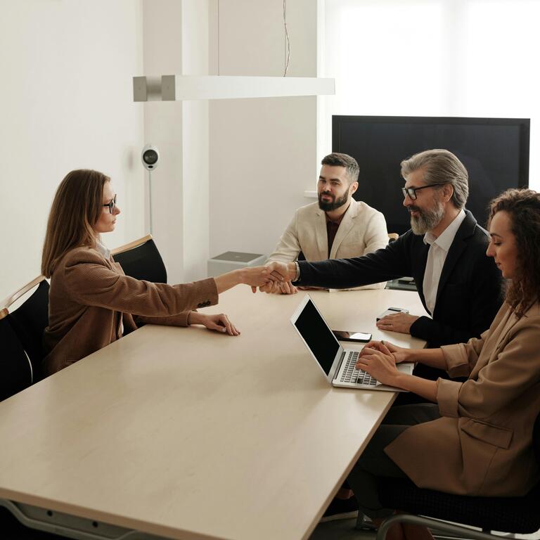 four employees are sitting on a desk and the man and woman are doing a handshake