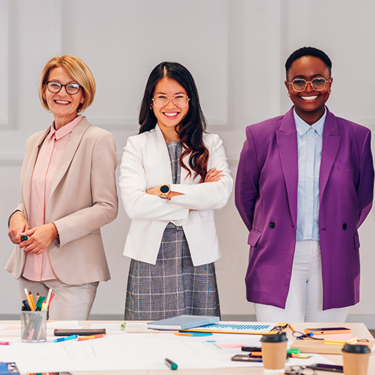 Group of adults both female and male of different ethnicities standing in a line, facing forwards whiles smiling