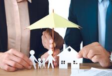 Two men holding paper houses and paper people with an umbrella over them