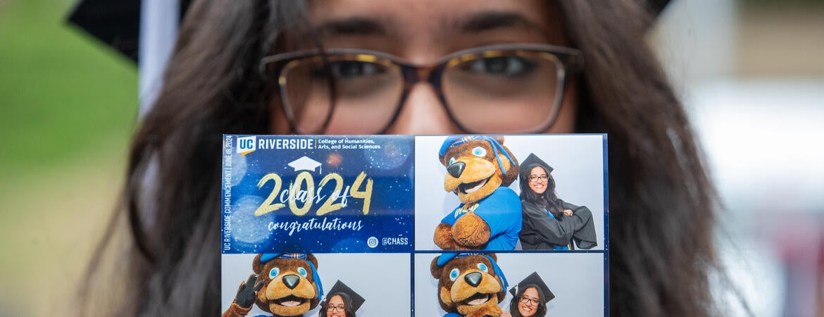 Graduate holding up photo of themself with UCR's mascot Scotty the Bear
