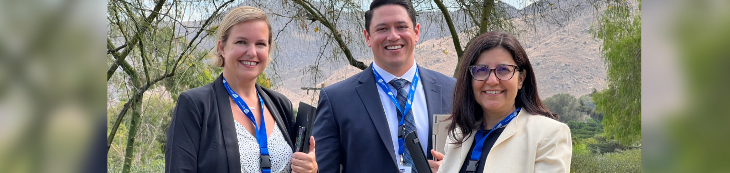 Three ITS staff members holding their laptops and smiling