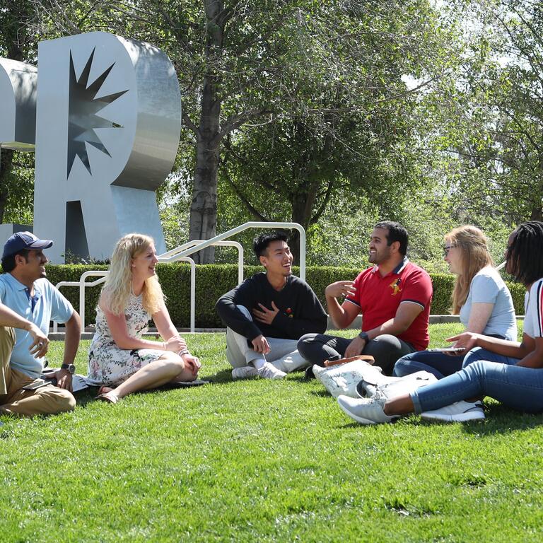 A group of students sitting on the grass by UCR letters
