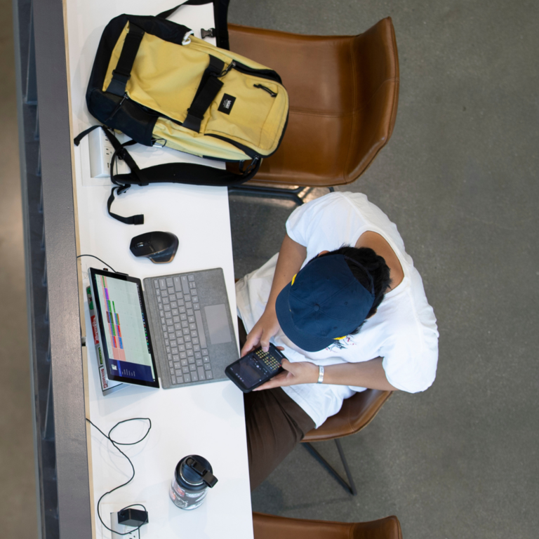 Student on laptop reviews phone while other students go up stairs.