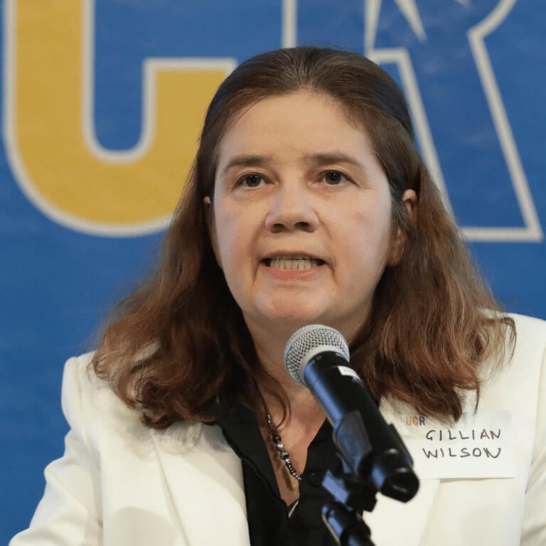A woman with brown hair in a lab coat speaking into a microphone