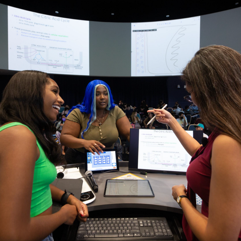 Two students and a faculty member stand next to a tablet 