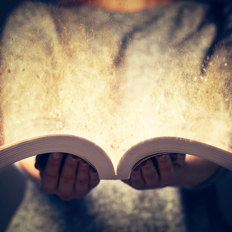 A person holds an open book and glowing light emerges from the pages