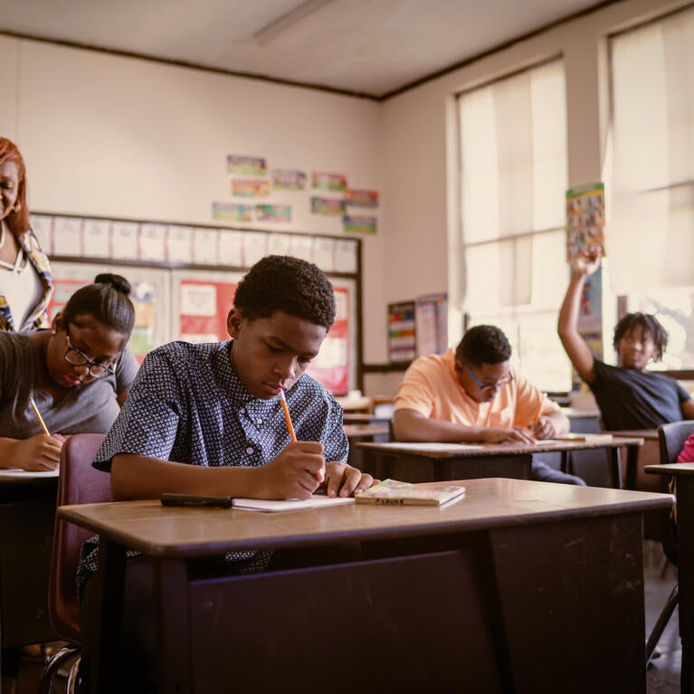 A teachers walks among students doing work at their desks.