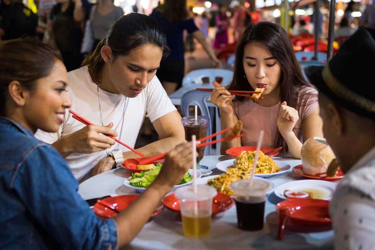 Group of friends sitting around a small table, eating various foods.